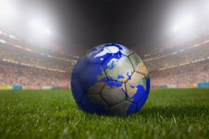 Soccer ball painted like a globe resting on grass in large stadium